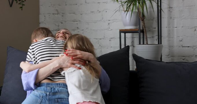 Two kids runs and hug mother on comfortable couch at home living room, happy laughing mom with adorable loving daughter and son. Mothers day, birthday celebration