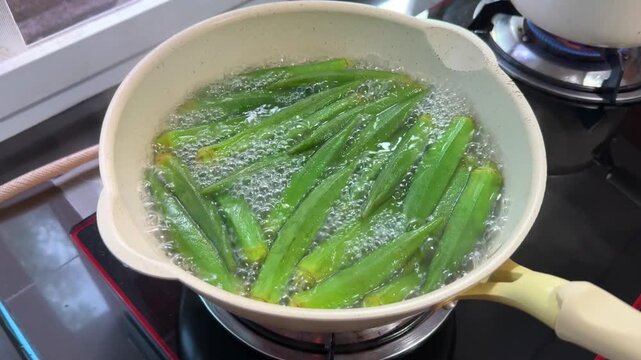 My MovieClose-up of fresh okra boiling in pot with bubbling water. Shows simple healthy cooking process using natural vegetables in home kitchen.
