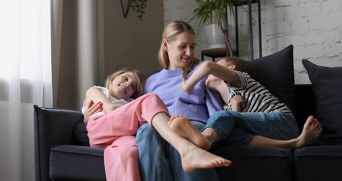 Mother with two kids on having fun cozy couch at home living room. Mom with adorable loving daughter and son spending time together. Family bonding