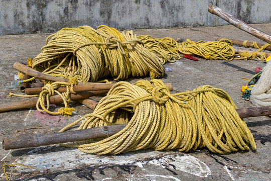  A detailed view of thick yellow coiled fishing rope and wooden poles scattered across a seaside dock or coastal fishing area. Showcasing traditional marine equipment of fishermen and harbour life.