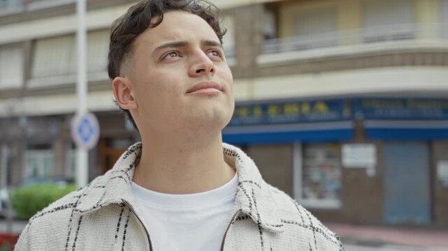 Man face gazing upward on a street, bare neck visible, wearing white tshirt and checked jacket; hopeful reflection.