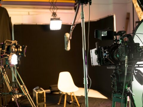 Inside a contemporary filming studio, cameras and lighting gear are set up, preparing for an engaging podcast or interview