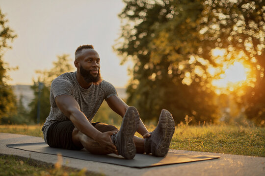 Man stretching hamstrings on yoga mat outdoors during golden hour with warm sunlight in natural park setting promoting fitness wellness and healthy lifestyle