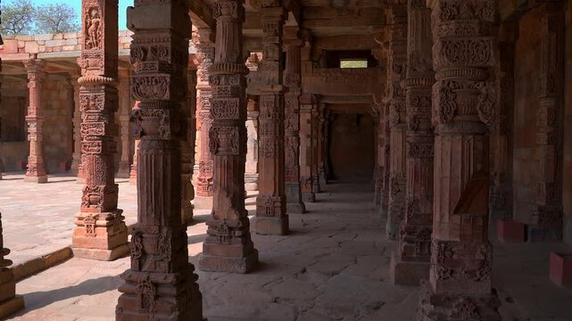 A static shot from within a colonnade at the Qutb Minar complex in New Delhi, featuring a rhythmic perspective of ancient red sandstone pillars decorated with detailed traditional carvings