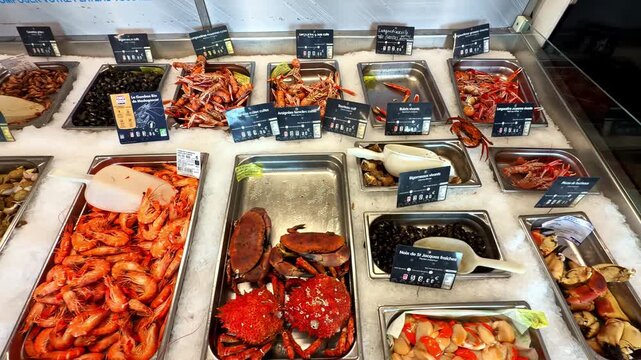 Fresh seafood arranged in metal trays on ice with price signs at market counter, Cancale, France