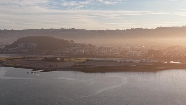 Morning aerial footage capturing the hazy sunrise over the San Francisco Bay, highlighting Albany Beach and the hills near Berkeley, California, with golden light filtering through the mist