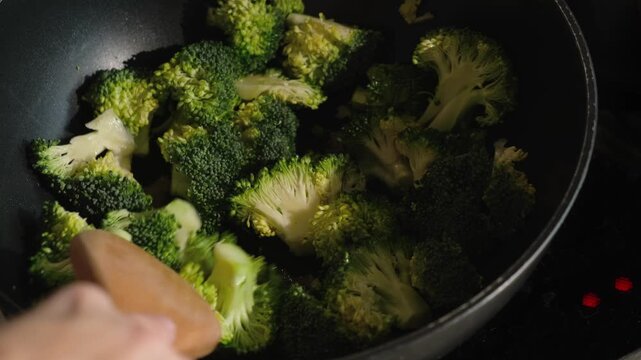Woman frying broccoli in pan. Cooking plant based meal, healthy vegetarian or vegan food.