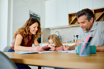 Fototapeta premium Parents cheerfully helping their young daughter with school homework, supporting her education while learning together at home