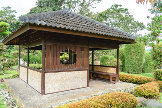 Traditional wooden pavilion in a lush tropical garden with tiled roof and open seating area, reflecting calm and cultural outdoor architecture.