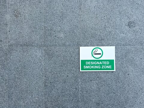 A green and white designated smoking zone information sign mounted on a grey granite stone wall in a public area.