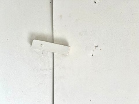 A simple white wooden bar latch screwed onto a white wall or door as a temporary locking mechanism.