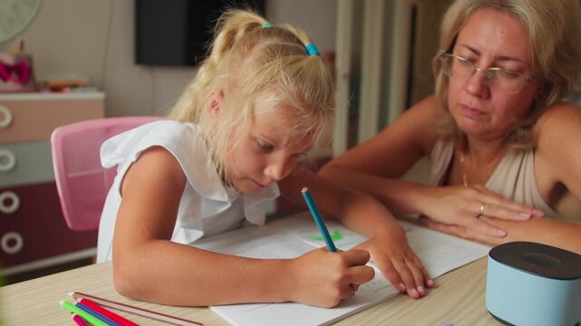 Preschool girl doing homework at home with mother support. Preparing for school through early learning and daily study routine