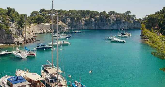 Yachts and sailboats resting in calm waters of Calanque de Port-Miou, France. Coastal environment with cliffs, forest and clear sea