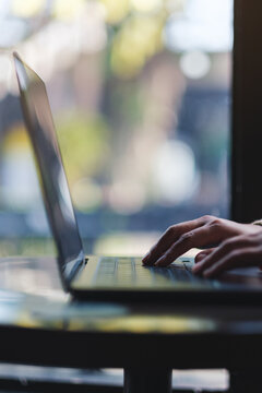 Vertical closeup image of a woman working and typing on laptop computer in cafe