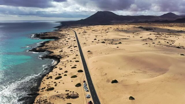 A long, straight road goes through a desert with clear skies above. The landscape is dry with few plants and mountains in the distance. It shows a vast and open area without people.