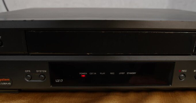 Video cassette tape coming out of VHS player in close-up shot. Retro media device and analog home video technology