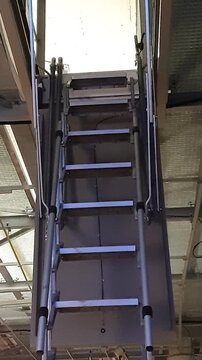 Deployed pull down, hatch or attic ladder coming down from a hung ceiling on a construction site. Vertical video.