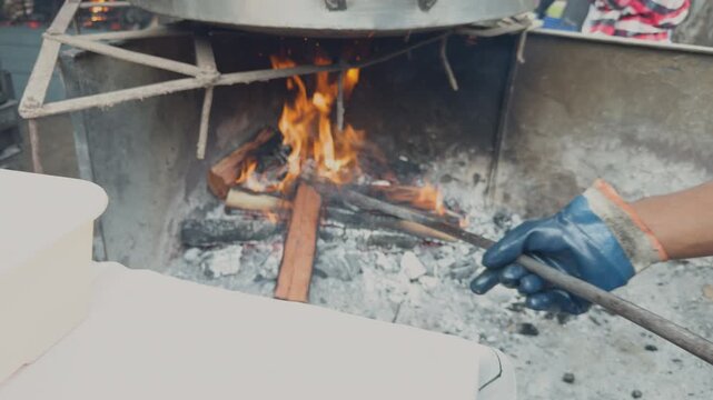 Person cooking outdoor with firewood and a large pot