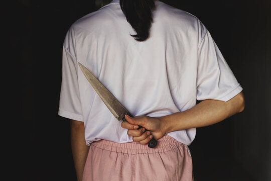 Silent Threat: Woman Concealing a Large Knife Behind Her Back