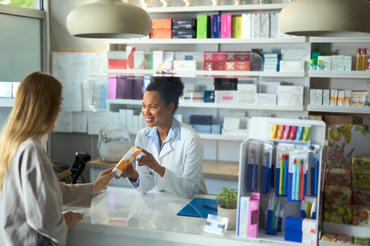 Happy black female pharmacist talking to her customer about moisturiser in a pharmacy.