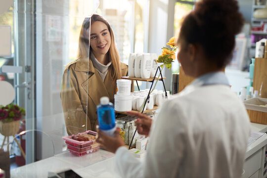 Happy young woman talking to a pharmacist while buying a medicine in a drug store.