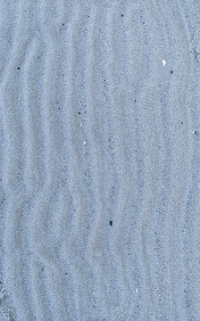 Close-up of fine sand with soft wave patterns. Minimal natural background texture for design and summer concepts.