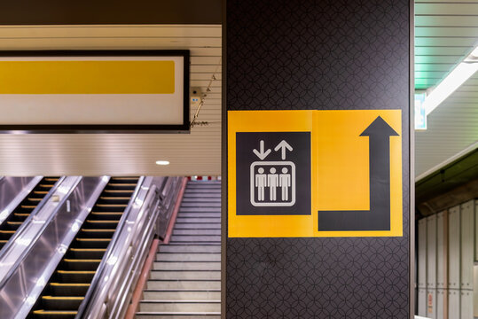 Elevator directional sign with arrow inside a modern Japanese train station next to an escalator. Concept of urban wayfinding, navigation system and public transportation facility in Tokyo.