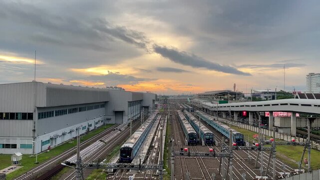 A wide-angle view of a railway depot at sunset shows multiple blue trains aligned on parallel tracks stretching into the distance.