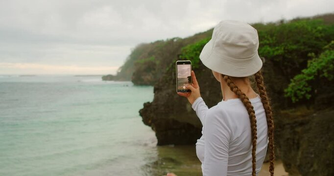 Solo traveler woman photographing coastal cliff and ocean for mindful travel in tropical Asia