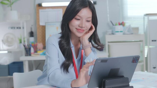 Smiling Asian Woman Working with tablet at a desk. businesswoman working from home, smiling and looking at screen. CEO businesswoman using tablet touchscreen tab device 