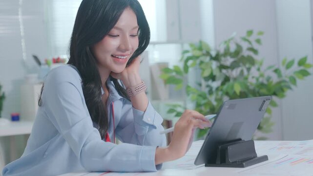 Smiling Asian Woman Working with tablet at a desk. businesswoman working from home, smiling and looking at screen. CEO businesswoman using tablet touchscreen tab device with pen