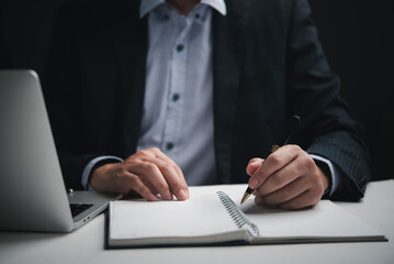 Fototapeta premium Hand businessman suit writing note brainstorming business idea strategy planning laptop dark office overtime executive working focused.