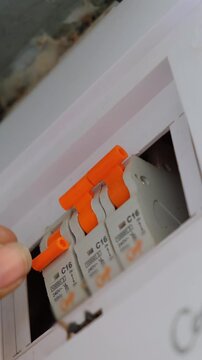 Close-up of a technician's hand switching an orange MCB lever in a residential circuit breaker panel
