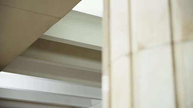 Minimalist interior architecture with a tiled stone column and repetitive white ceiling beams, highlighting geometric lines, natural light, and structural details in a corridor