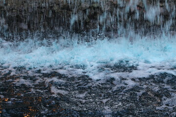 Close-up of cascading water with vibrant blue foam and dark ripples © khomkrit