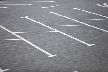 Fototapeta premium High-angle view of white painted parking lines and directional arrows on a gray paving stone surface at an empty outdoor parking area