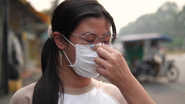 Side view of a young Asian girl wearing a protective face mask for PM 2.5 and air pollution prevention on a hazy city street background