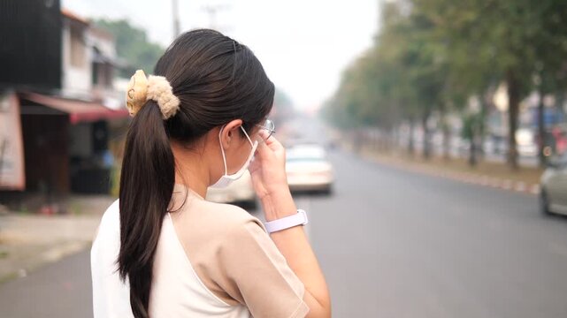 Back view of a young girl wearing a protective face mask looking at a foggy and polluted city road, PM 2.5 air pollution and environmental crisis concept