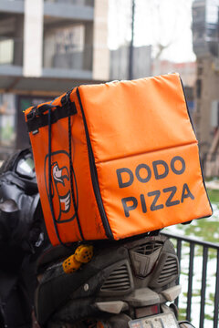 Tbilisi, Georgia - March 27, 2026: Vertical street city photo close up. Orange thermo bag for delivery food, drink with Dodo pizza logo on scooter luggage rack on parking lot. Concept of lunch, dinner