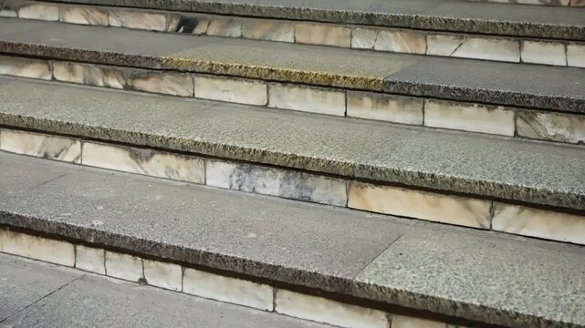 Close-up view of weathered stone staircase with textured granite treads and marble risers, showcasing age, stains, and urban wear across repeating steps in an outdoor setting