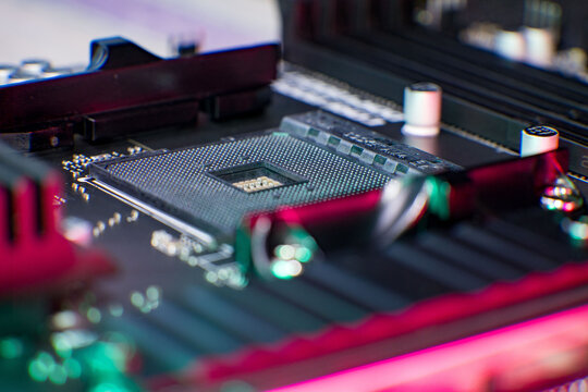 Detailed macro image showcasing an empty CPU socket on a computer motherboard, surrounded by capacitors and memory slots. RGB lighting highlights the intricate electronic components, emphasizing the p