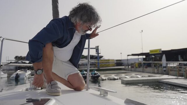 Mature man tying rope on a yacht at the marina