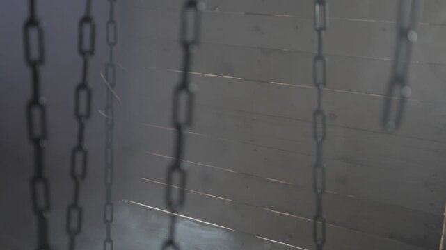 In a dark and smoky room full of hanging chains, a light comes through the holes in the wood wall announcing something ominous is comming