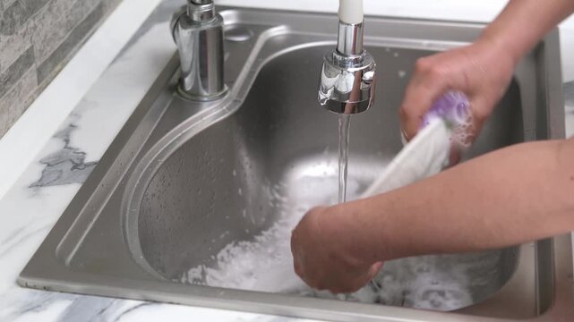 Washing a white plate in a kitchen sink using a sponge and soapy foam