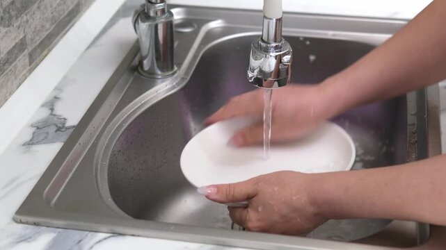 Washing a white plate in a kitchen sink using a sponge and soapy foam