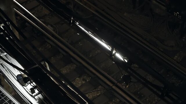 Dimly lit underground subway tracks with dense cabling, signals, and sleepers, revealing industrial infrastructure and electrical systems powering urban transit in a tunnel