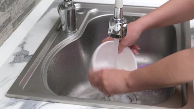 Washing a white mug in the kitchen sink using a sponge and soapy water