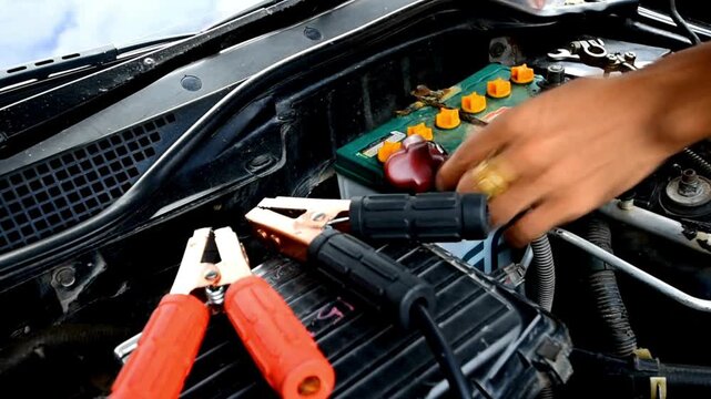 Mechanic hands connecting jumper cables to car battery terminals closely
