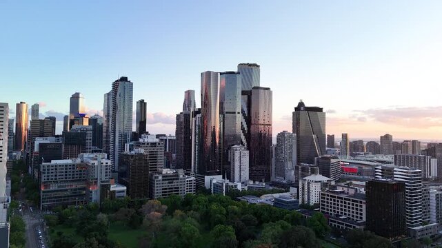Drone footage of Melbourne CBD skyline at sunset with modern skyscrapers, city buildings and stadium district under a colourful evening sky in Melbourne, Australia.
