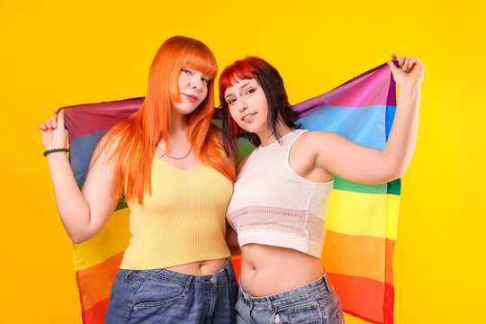 Lovely lesbian couple with rainbow flag on yellow background. LGBT concept